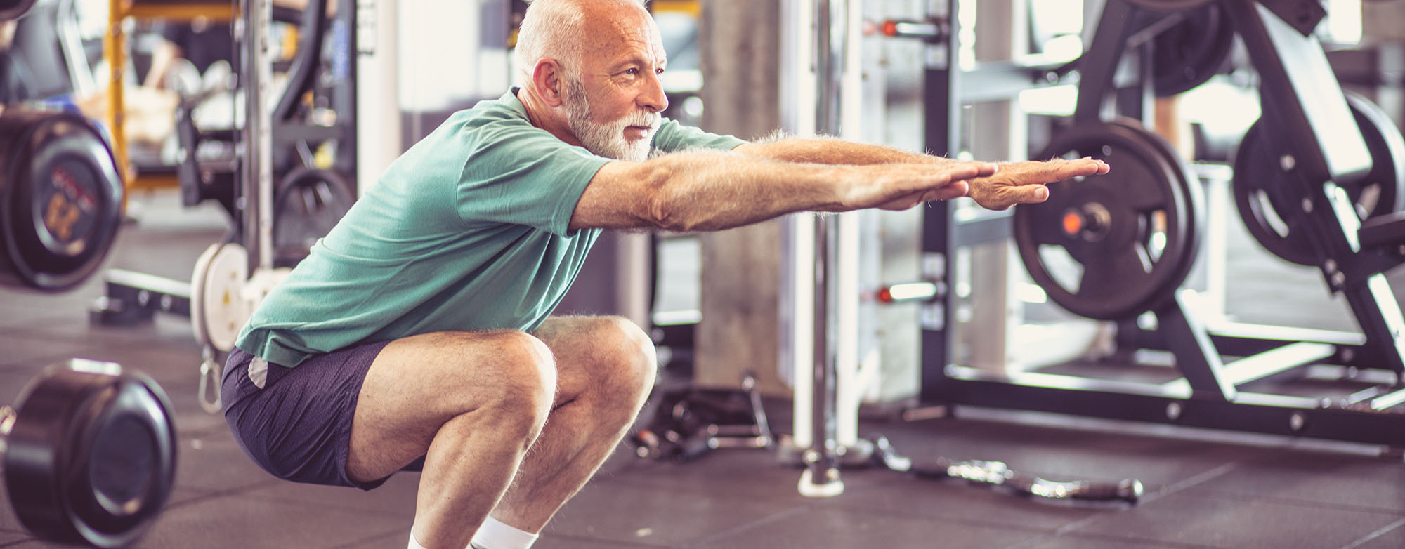 An elderly man squatting at the gym.